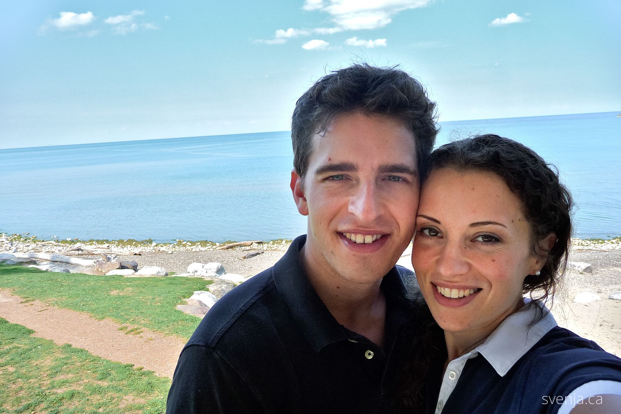 A couple looks at the camera with a lake in the background