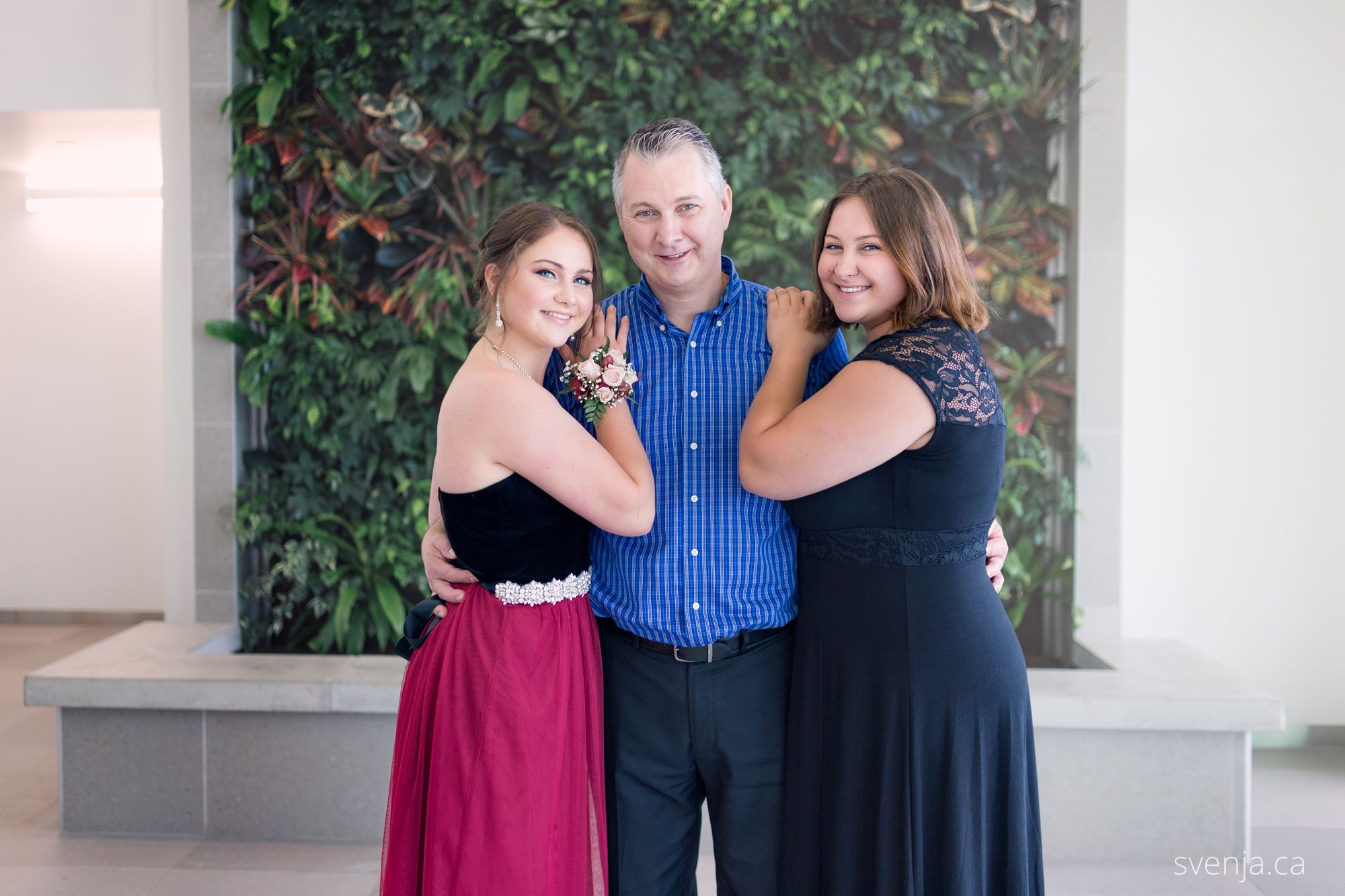 Dad with two daughters in front of a green plant wall