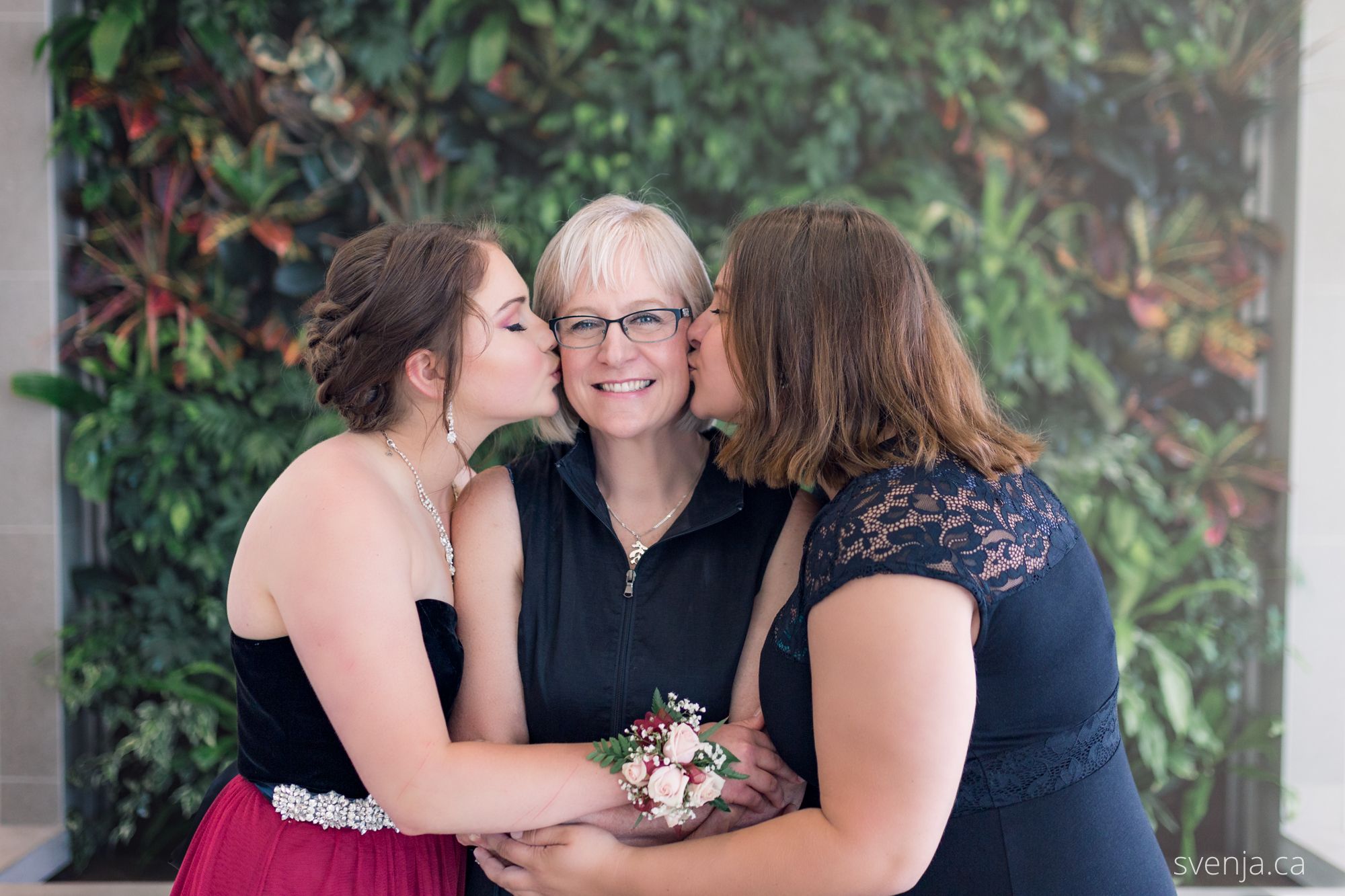 mom with two daughters in front of a green plant wall