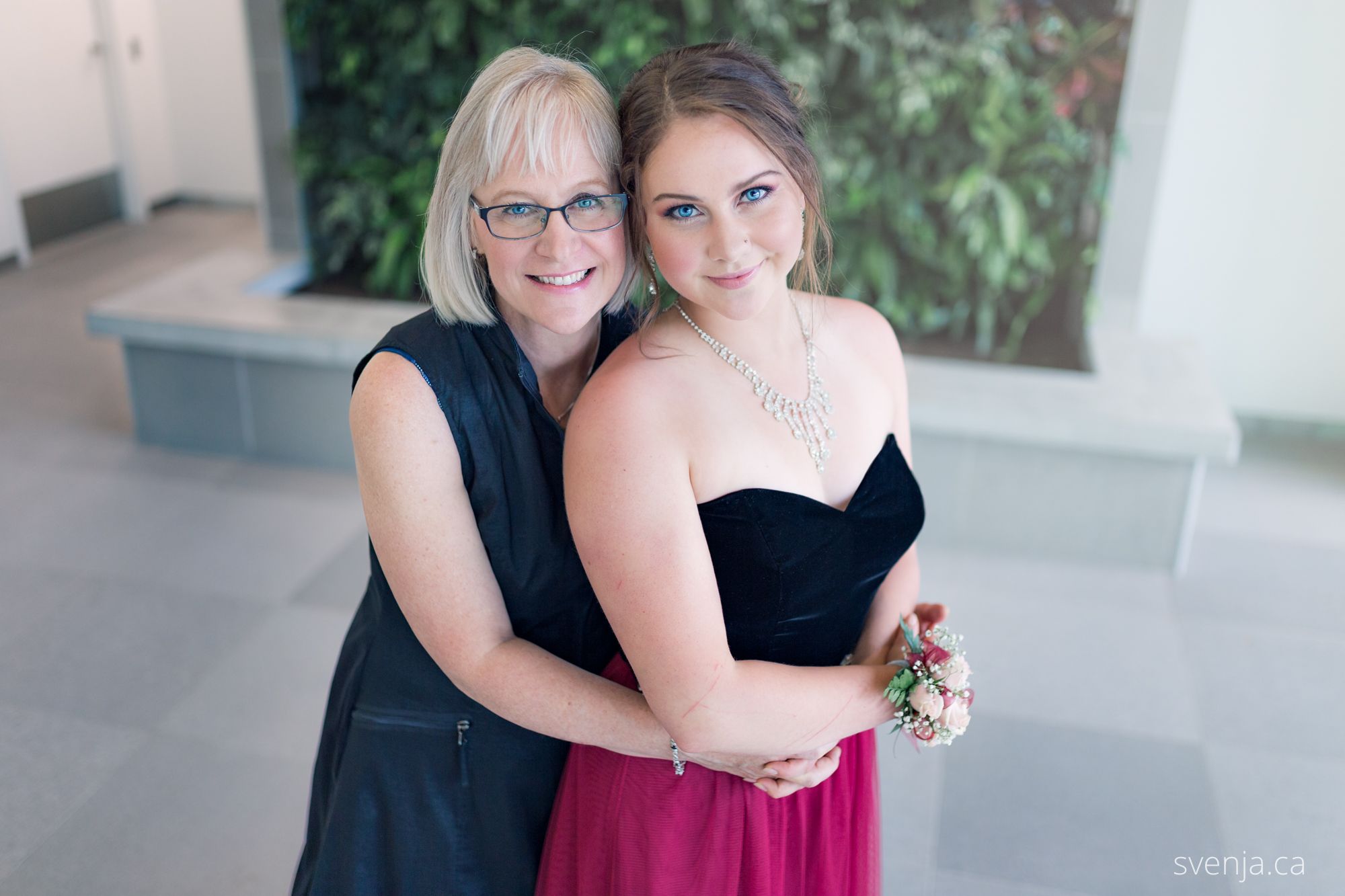 mother and daughter in front of a green plant wall