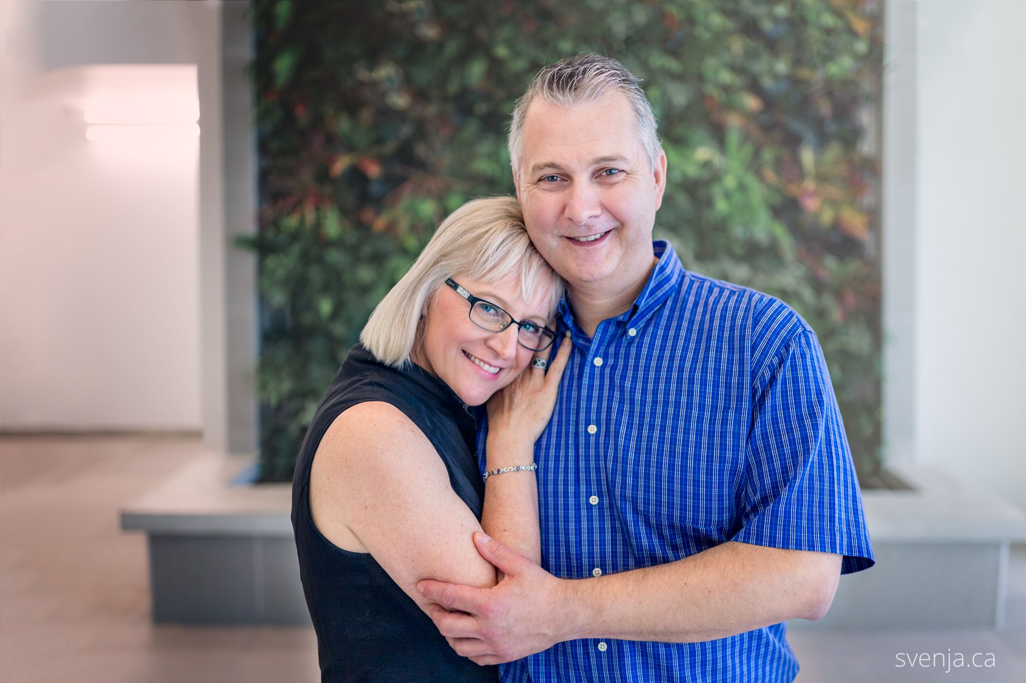 couple embracing in front of a green plant wall