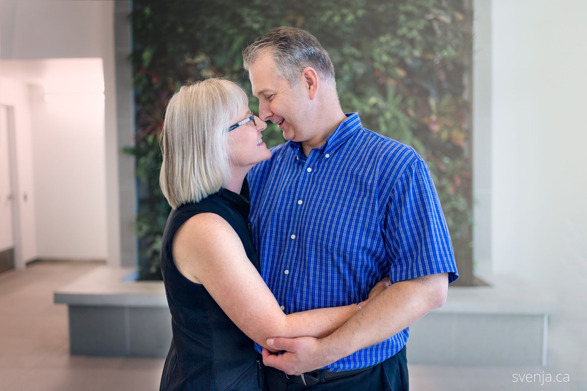 couple embracing in front of a green plant wall