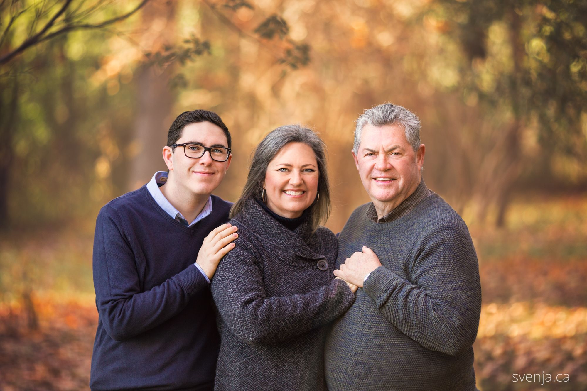 son, mother and father standing and smiling in front of trees