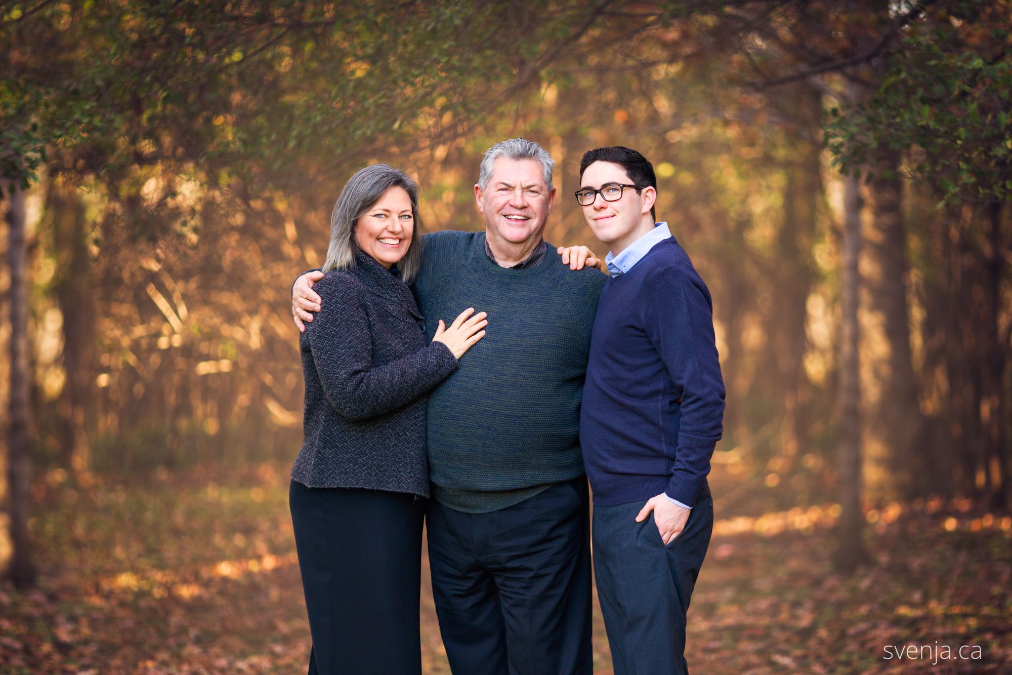 mother, father and son standing in front of trees