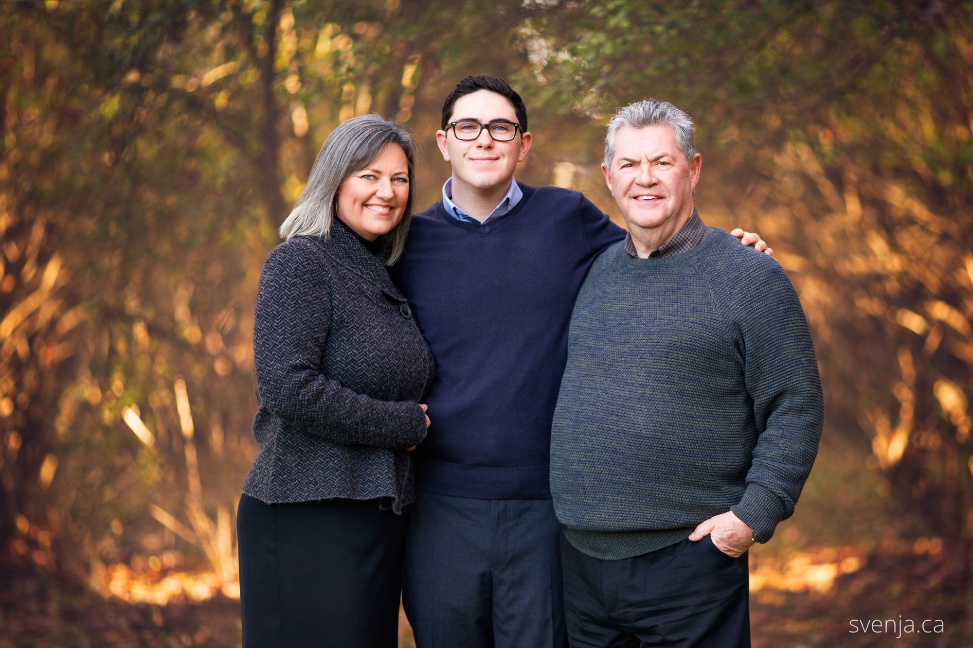 mother, son and father standing in front of trees smiling