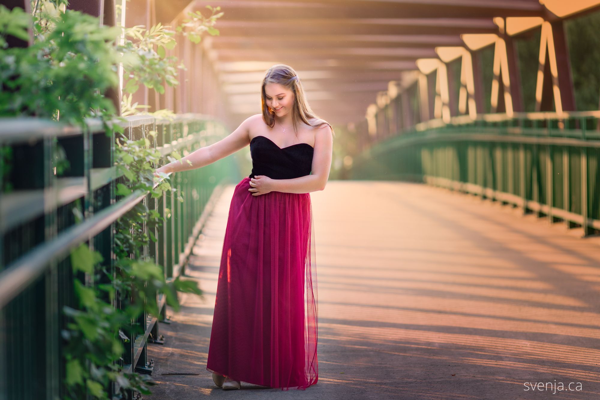 young woman in dress stands on a bridge with light beaming from the left