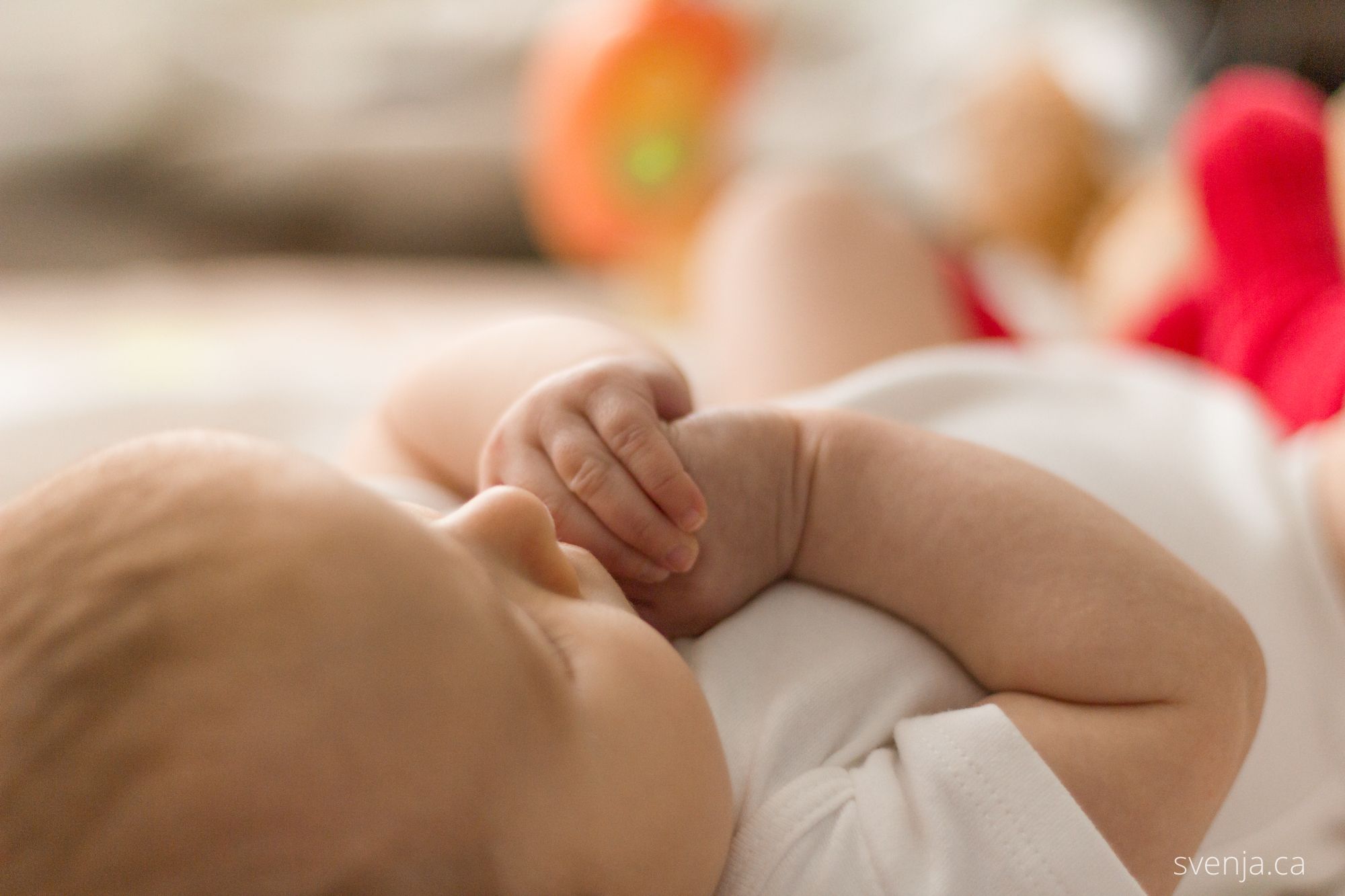 A baby holds her hands in her mouth while laying on her back