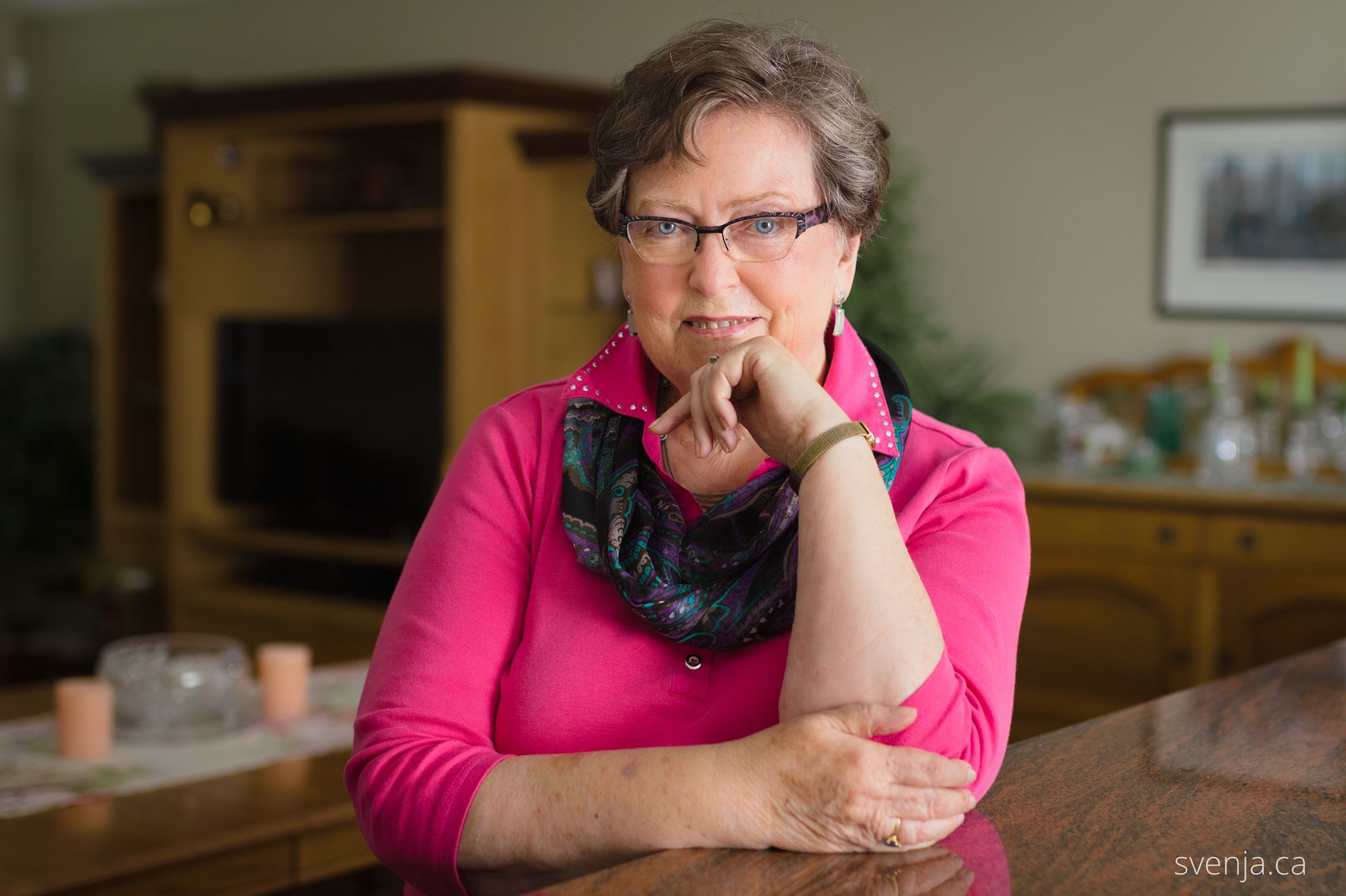 A woman faces the camera while leaning on a table