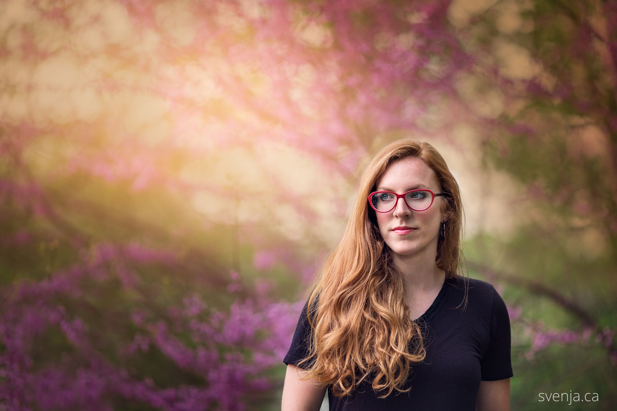 woman with red glasses looks to her right with blossoms in the background