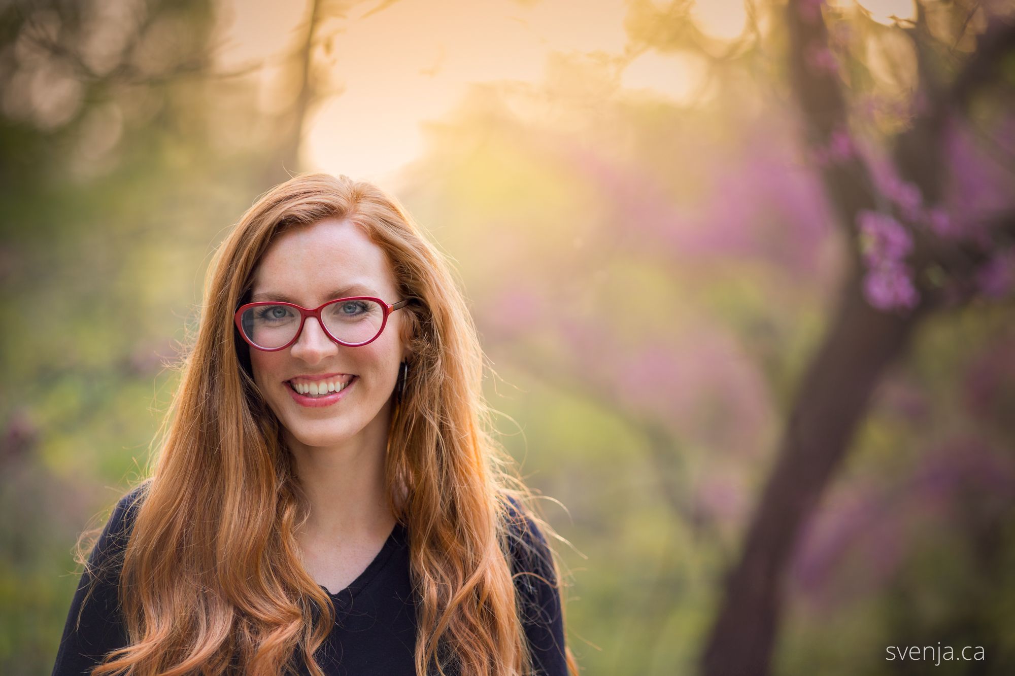 woman with red glasses smiles with blossoms in the background