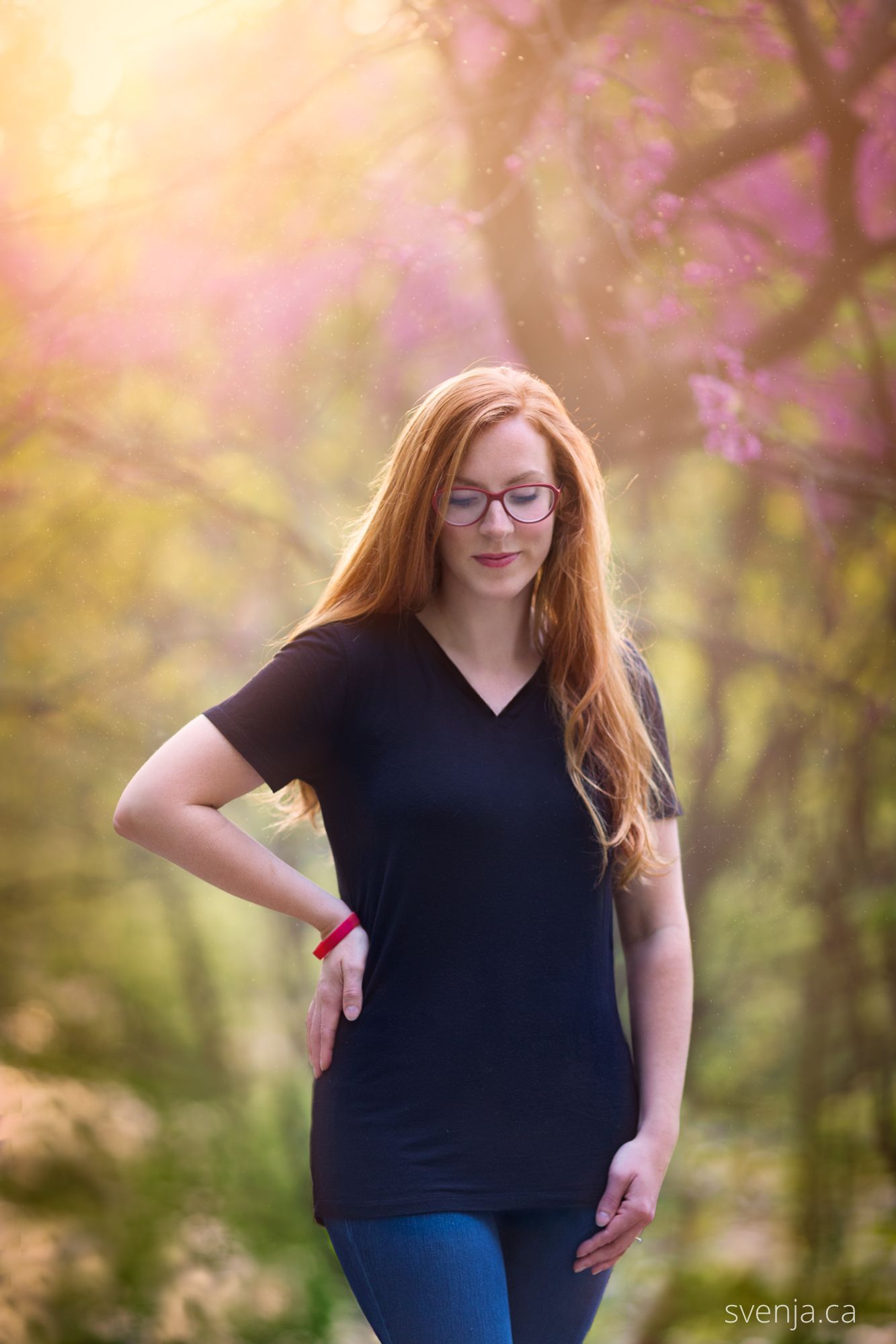 woman with red glasses looks down while walking with blossoms in the background